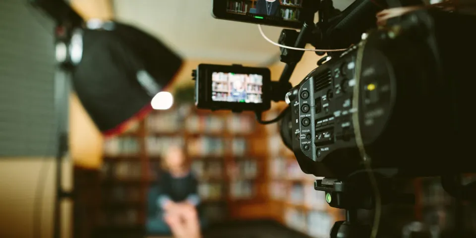 Cámara de video grabando una entrevista en un estudio con una biblioteca al fondo