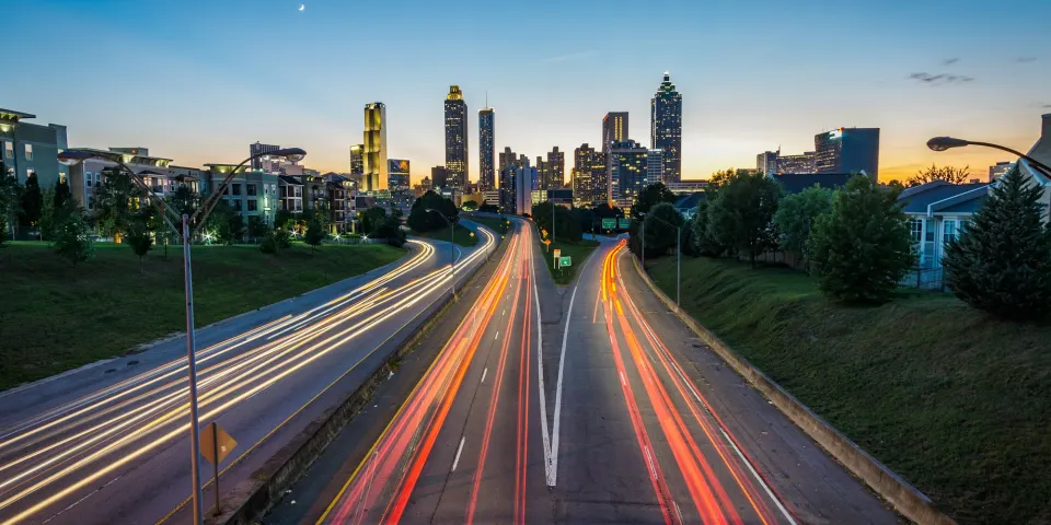 Autopista con estelas de luz de los carros al atardecer frente a una ciudad