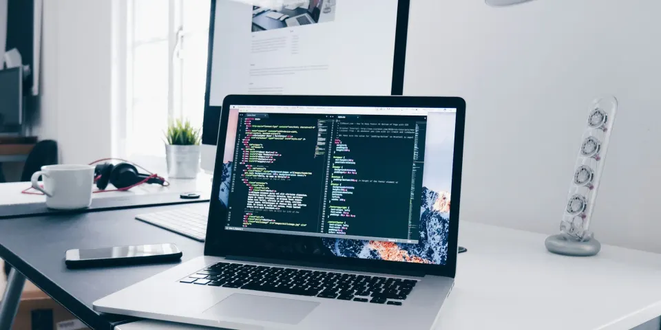 Computador portátil con código en la pantalla sobre un escritorio blanco junto a una taza de café
