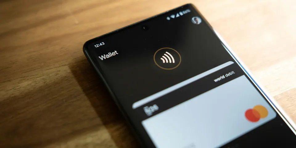 Celular con una billetera digital y una tarjeta en pantalla sobre una mesa de madera