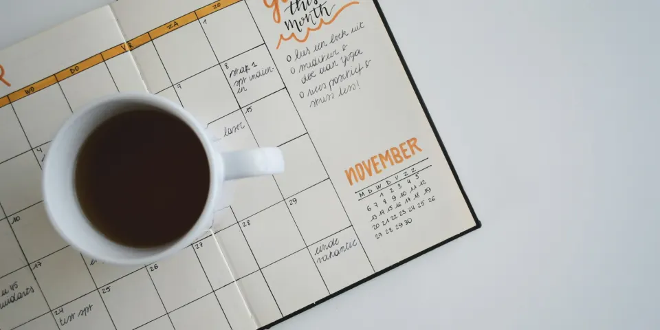 Agenda abierta con un calendario y una taza de café sobre la mesa