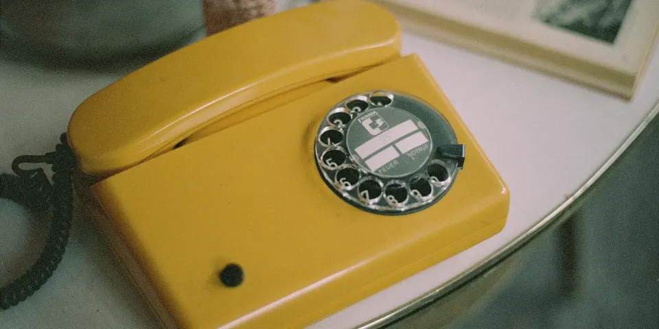 Teléfono amarillo antiguo de disco sobre una mesa junto a un libro abierto