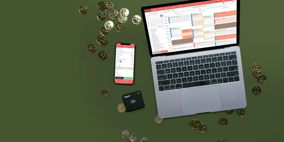 Computador portátil, celular y tarjeta rodeados de monedas sobre un fondo verde