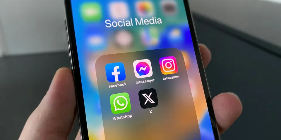 Mano sosteniendo un celular con una carpeta de aplicaciones de redes sociales en la pantalla