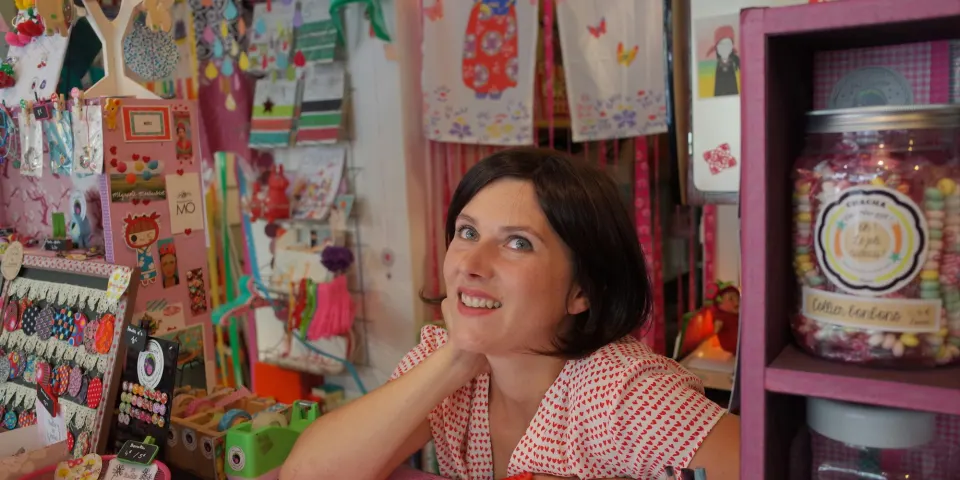 Comerciante pensativa apoyada en el mostrador de su tienda llena de productos de colores