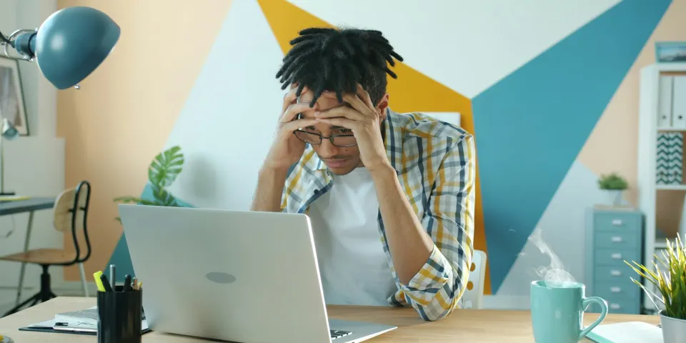 Hombre preocupado con las manos en la cabeza frente a su computador portátil