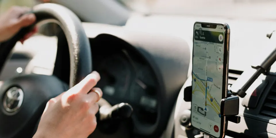 Conductor usando un celular con mapa de navegación montado en el tablero del carro
