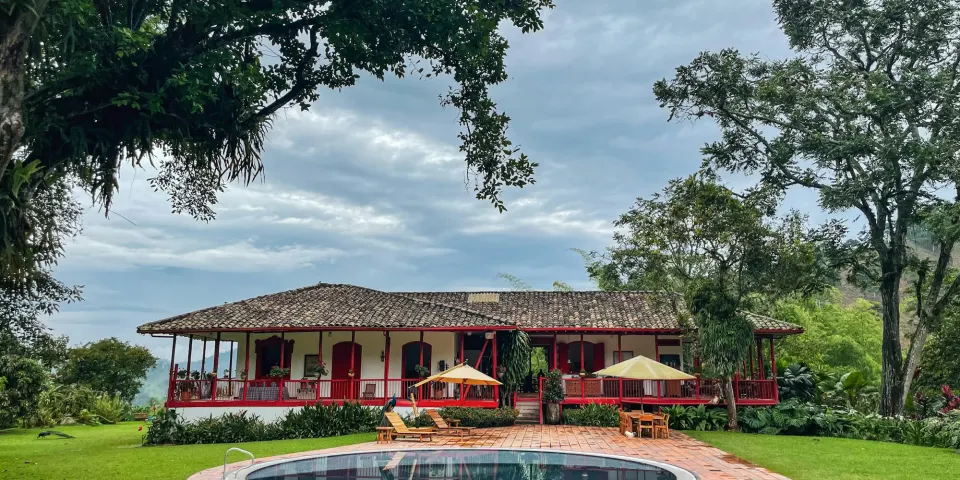 Casa de finca con corredores y piscina rodeada de árboles y jardines