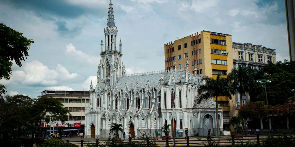 Iglesia gótica blanca rodeada de edificios y palmeras en el centro de una ciudad