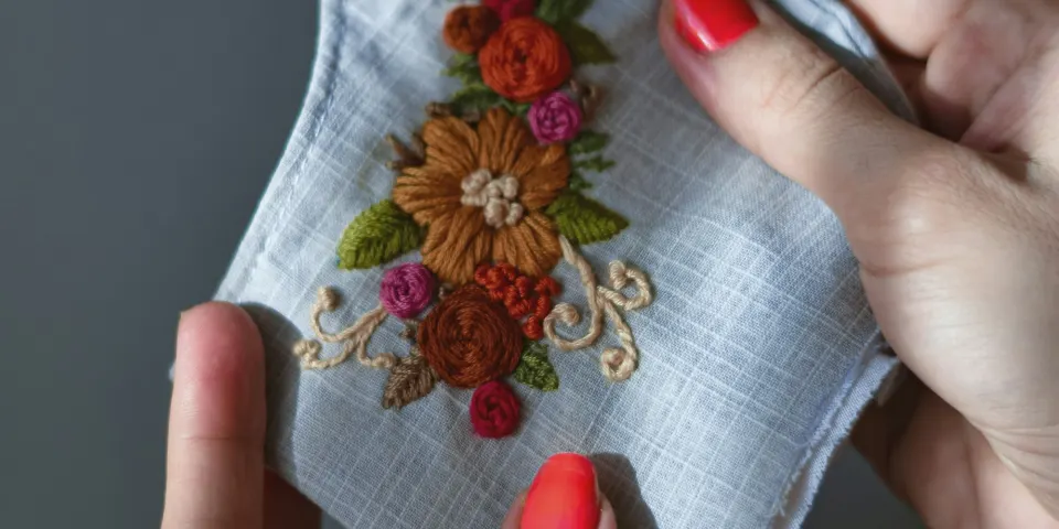 Manos bordando flores de colores sobre una tela blanca