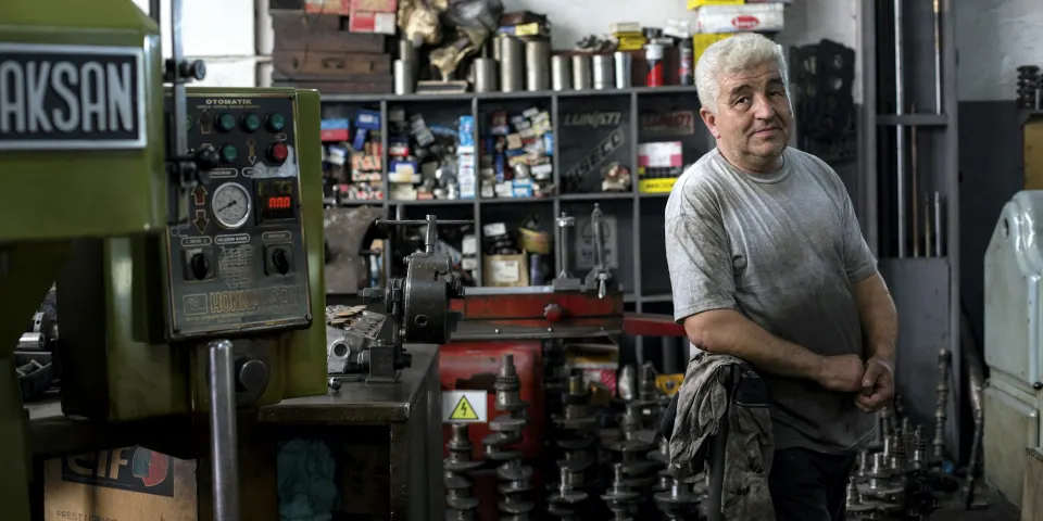 Dueño de un taller metalmecánico de pie junto a sus máquinas