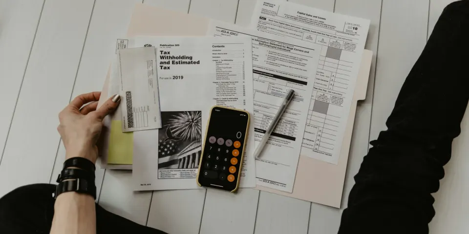 Manos revisando formularios de impuestos con una calculadora en el celular