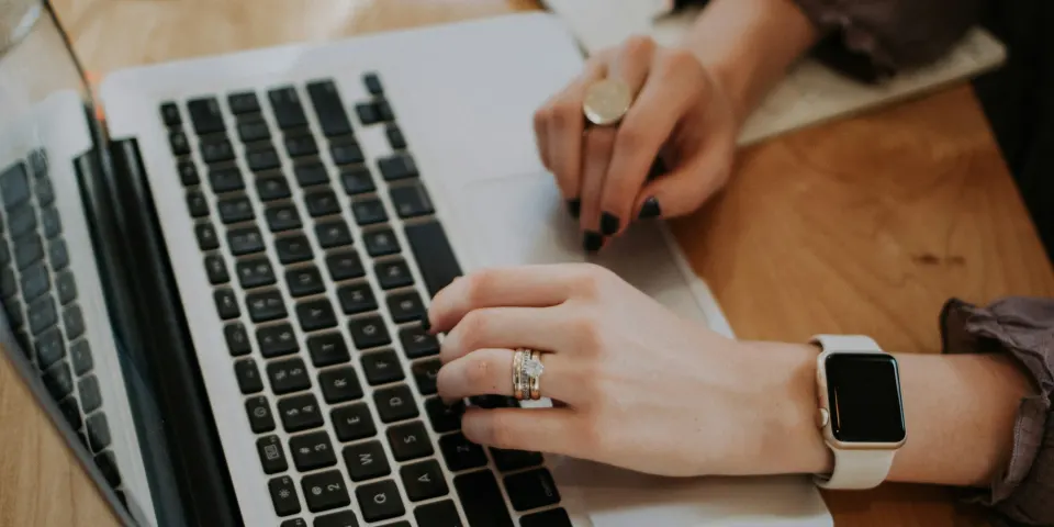 Manos de una mujer escribiendo en un computador portátil sobre una mesa de madera