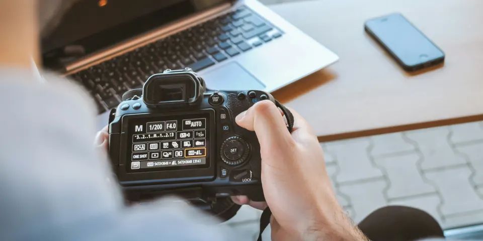 Fotógrafo revisando fotos en su cámara frente a un computador portátil