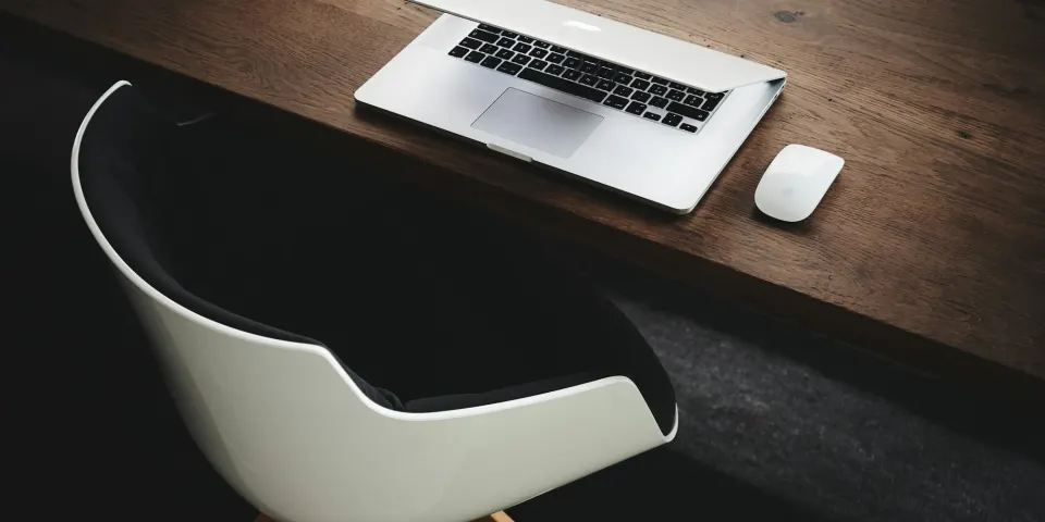 Computador portátil cerrado sobre un escritorio de madera oscura junto a una silla blanca