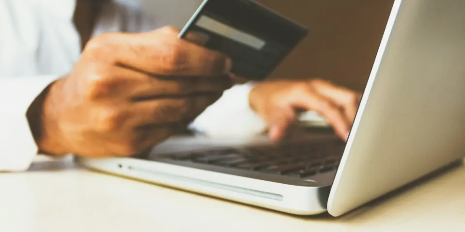 Persona sosteniendo una tarjeta de crédito mientras compra desde su computador portátil