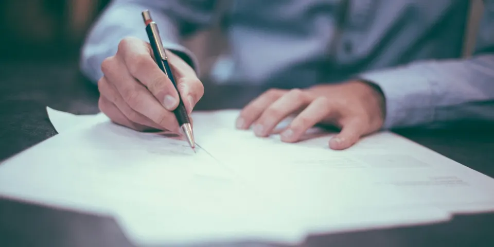 Persona firmando un documento sobre un escritorio