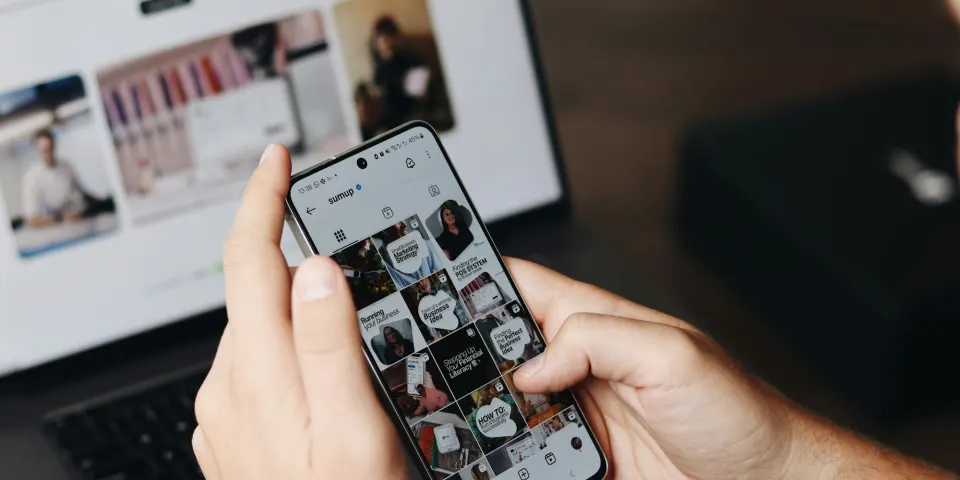 Persona revisando un perfil de Instagram en su celular frente a un portátil con una página web abierta