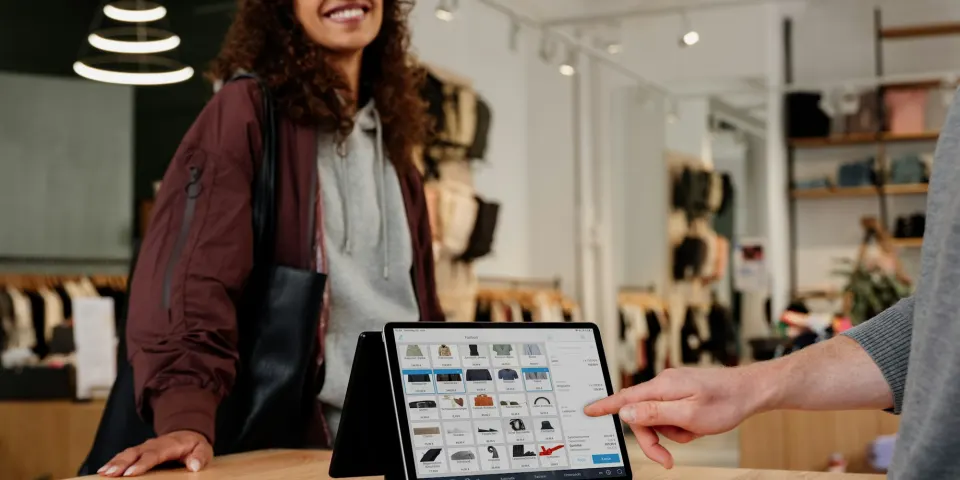 Cliente sonriente en el mostrador de una tienda mientras le muestran productos en una tableta